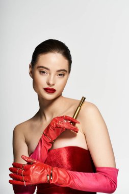 Çarpıcı bir kadın, altın bir nesneyi nazikçe tutarken, çarpıcı kırmızı bir nesneyle güzelliğini sergiliyor..