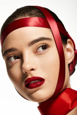 Kalın kırmızı dudaklı bir kadın entrikayla, zarif bir şekilde kırmızı kurdeleyle bakar..