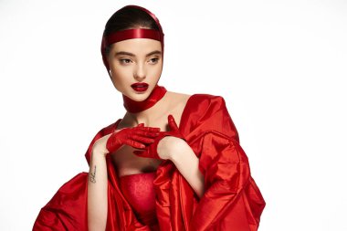Canlı kırmızı kumaşla süslenmiş çarpıcı bir kadın zarif bir şekilde sanatsal bir şekilde poz veriyor..
