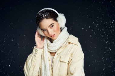 Çekici bir bayan, gülümseyerek rahat bir eşarp ve kulaklıkla kış atmosferinin tadını çıkarır..