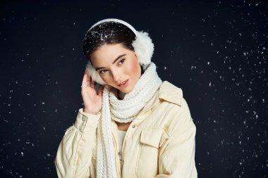 A charming lady enjoys the winter atmosphere with a cozy scarf and ear muffs while smiling. clipart