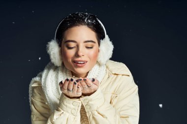 A joyful woman in winter attire gently catches snowflakes with her hands during a snowy evening. clipart