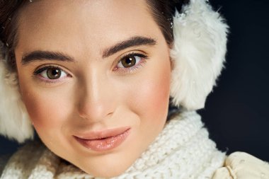 Güzel bir kadın sıcak bir şekilde gülümser, kışlık kıyafetler giyer, serin bir atmosferde neşe saçar..
