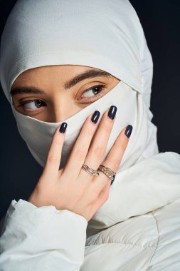 Bir kadın nazikçe yüzüne dokunur, başörtüsü takarken zarafetini gösterir..