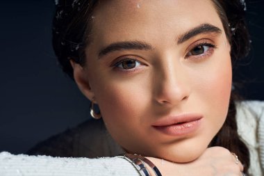 Genç bir kadın, kış modasında doğal güzelliğini sergileyerek çenesini eline dayar..