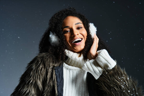 A stylish African American woman smiles brightly while showcasing winter fashion with earmuffs and a warm sweater.