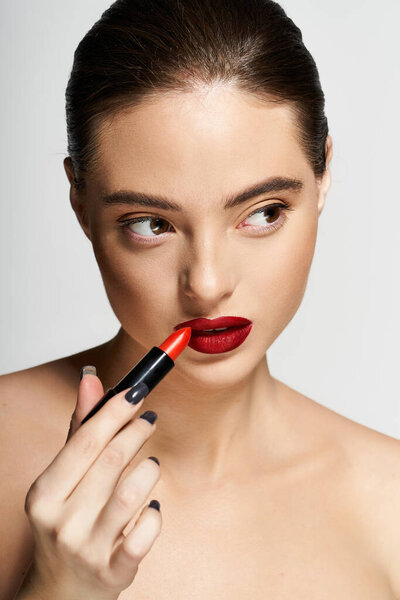 С целенаправленным выражением лица, красивая женщина увеличивает губы ярко-красной помадой.