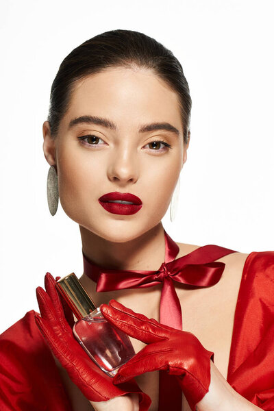 Элегантная женщина, одетая в яркий красный наряд, демонстрирует бутылку духов с самообладанием и красотой..