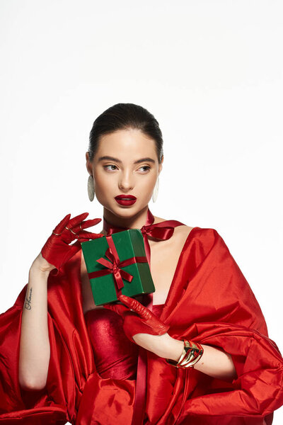 The elegant woman dressed in vibrant red showcases a small green gift box during a joyful event.