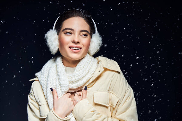 Среди падающих снежинки, женщина обнимает зимний холод в теплой одежде и наушниках.