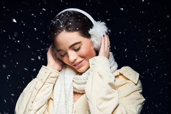 Радостная женщина обнимает зимний холод, тихо улыбаясь, пока вокруг нее танцуют снежинки..