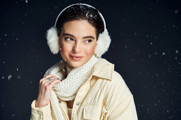 Стильная женщина счастливо улыбается, когда снежинки мягко падают вокруг нее зимой..