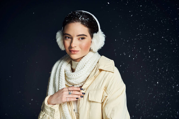 Молодая женщина тихо улыбается, окруженная падающими снежинками, одетая в уютный зимний наряд.