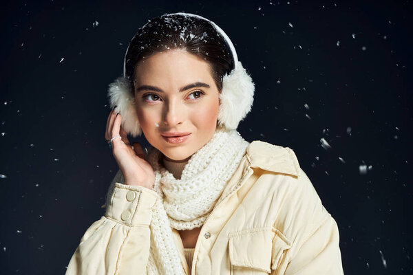 Женщина игриво касается ее уха, в то время как снежинки мягко падают вокруг нее в теплой обстановке.
