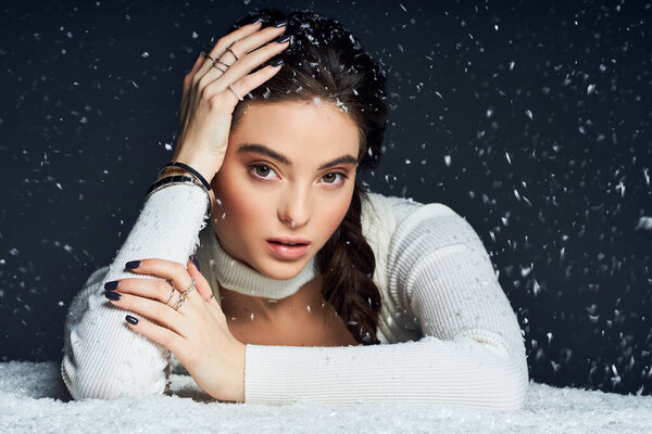 Потрясающая женщина изящно лежит с рукой на голове, окруженная падающими снежинками..