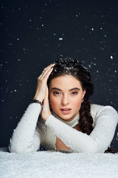 Красивая женщина с темными плетеными волосами изящно позирует, окруженная падающими снежинками.