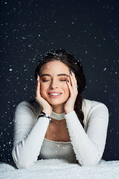 A happy woman embraces a flurry of snowflakes while smiling joyfully in a warm setting.