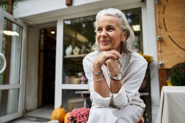 Güzel, olgun bir kadın dışarıda, güneşin sıcaklığını kucaklayarak mutlu bir şekilde oturur..