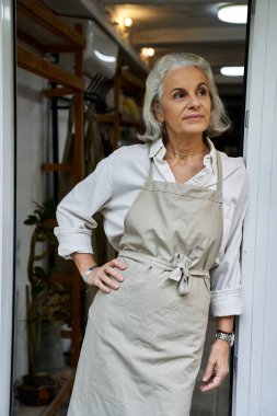 Açık renk elbiseli düşünceli bir kadın kapının önünde duruyor, yaratıcılık ve deneyim yayıyor..