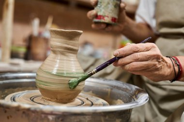 A talented craftsman uses a brush to decorate a new pottery creation with earthy tones. clipart