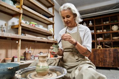 Yetenekli olgun bir kadın, yaratıcı aletlerle çevrelenmiş vaziyette çanak çömlek şekillendirir ve dekore eder..