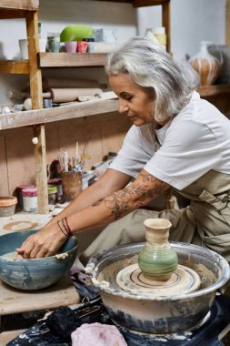 A skilled woman shapes clay on a potters wheel, surrounded by tools and artistic creations. clipart