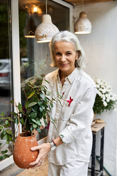 A lovely woman enjoys gardening while holding a potted plant outside her quaint home.