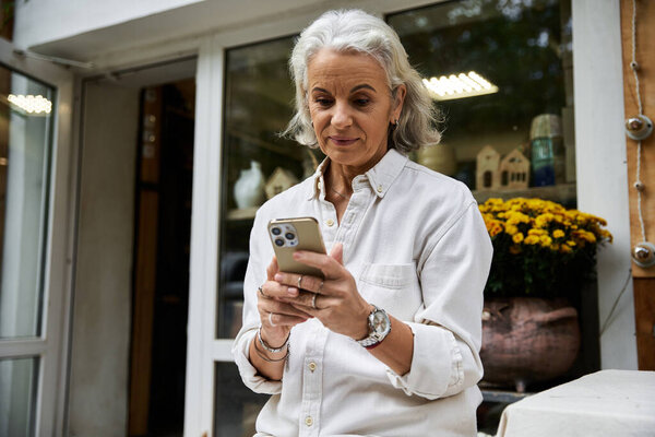 A graceful mature woman engages with her smartphone while enjoying a serene outdoor space.