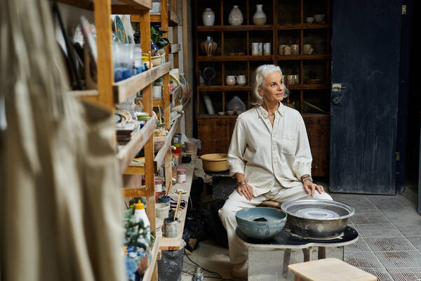 Элегантная зрелая женщина сосредоточена на гончарном деле посреди хорошо организованной студии.