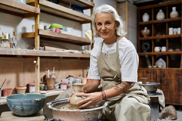 A skilled artisan is shaping a clay pot with care in her inviting workshop.