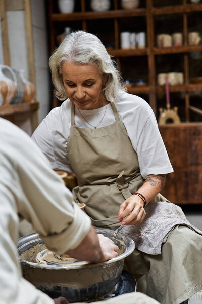 A mature woman crafts pottery at a tranquil studio, engaging deeply in her creative process.