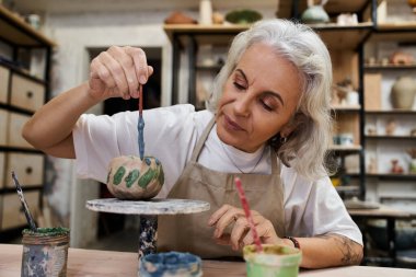 An expert craftswoman adds intricate details to a beautifully shaped bowl, showcasing creativity. clipart