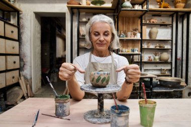 Mutlu bir zanaatkar, çeşitli sanat malzemelerinin arasında kilden güzel bir kap oluşturur..