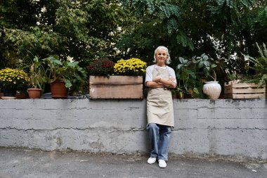 Güzel, olgun bir kadın, yemyeşil bahçesinde çiçeklerin arasında gururla durur..