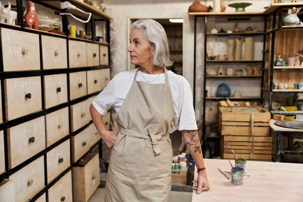 The mature woman, dressed in an apron, prepares to begin her creative work in a serene studio.