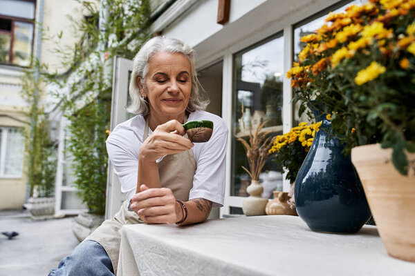Красивая зрелая женщина расслабляется за столом, наслаждаясь временем со своим любимым растением в саду.