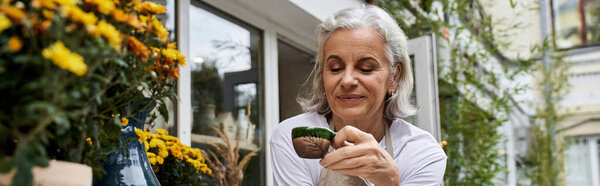 The woman smiles softly as she carefully examines her plants, surrounded by bright blossoms.