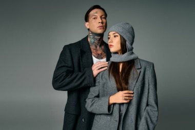 Modayı takip eden genç bir çift birbirine yakın duruyor. Gri tonlarda modern moda sergiliyorlar..