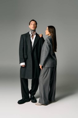 A young couple exudes confidence with their chic gray attire in a modern studio setting. clipart