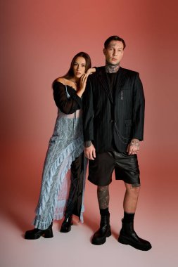 Genç bir çift özgüvenle ayakta duruyor, dikkat çekici bir arka planla benzersiz moda seçimleri sergiliyorlar..