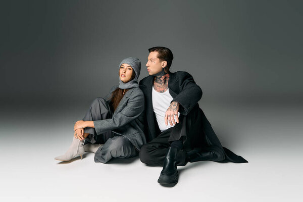 Модная пара позирует на ровном полу, демонстрируя свои шикарные наряды и татуировки.