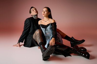 A young couple showcases their trendy fashion while sitting against a vibrant background.