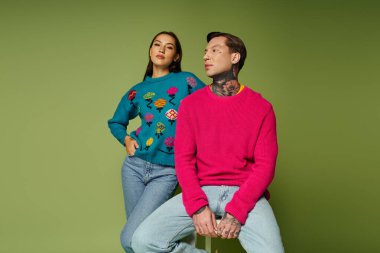 İki çekici şahıs, modern moda eğilimleri sergileyerek, renkli kazaklar içinde rahatça poz veriyorlar..