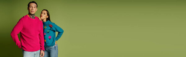 A stylish young couple showcases trendy sweaters while posing in front of a green backdrop.