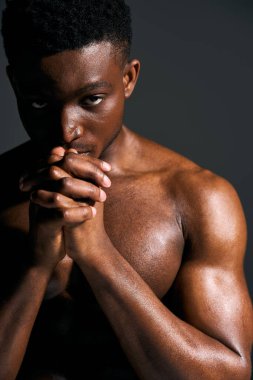 Genç, yakışıklı bir Afro-Amerikan erkeği güçlü vücudunu sergileyerek elleri sımsıkı bağlı üstsüz poz veriyor. Onun yoğun bakışları ve düşünceli ifadesi bir düşünce ve güç atmosferi yaratır..