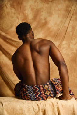 Genç, yakışıklı bir Afrikalı Amerikalı üstsüz ve kendinden emin bir şekilde poz veriyor. Arka plandaki sıcak ses tonları güçlü fiziğini vurgulayarak sanatsal ve ilham verici bir atmosfer yaratıyor..