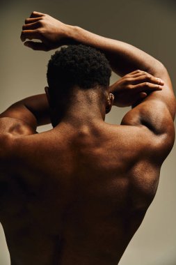 Genç ve yakışıklı bir Afro-Amerikan erkeği sırtı izleyiciye dönük duruyor ve heykel şeklindeki fiziğinin altını çiziyor..