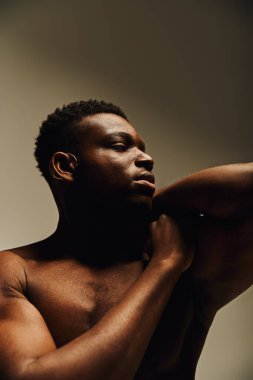 Genç, yakışıklı bir Afrikalı Amerikalı üstsüz poz veriyor, gücünü ve zarafetini sergiliyor. Yumuşak ışıklandırma onun özelliklerini geliştirirken aynı zamanda samimi bir atmosfer yaratır..