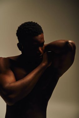 Genç ve yakışıklı bir Afrikalı Amerikalı üstsüz poz veriyor, atletik fiziğini iyi aydınlatılmış, minimalist bir ortamda sergiliyor..