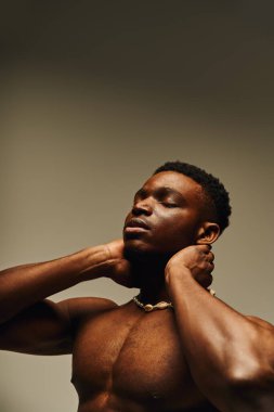 Genç ve yakışıklı bir Afro-Amerikan erkeği rahat bir ifadeyle poz veriyor, heykel şeklini ve kişisel tarzını sergiliyor..
